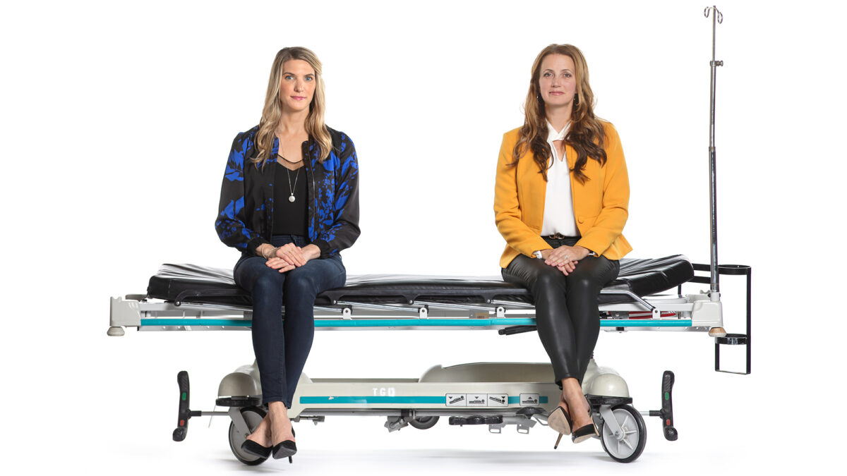 Patients Emily Fox (left) and Katie Shea sit on a stretcher together.